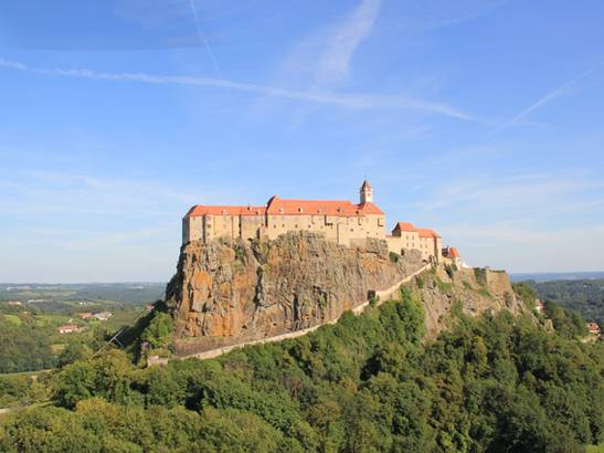 Burg auf einem Felsen mit grünem Wald im Vordergrund